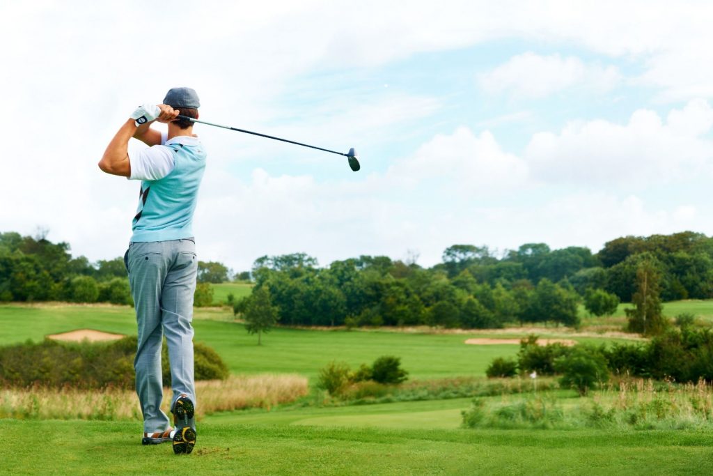 A man swinging a gold club at a gold course